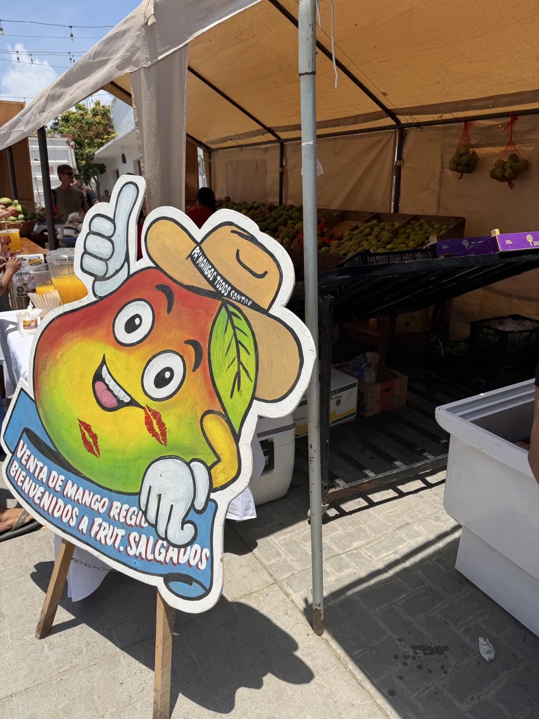 A colorful mango character sign in front of crates of fresh mangoes